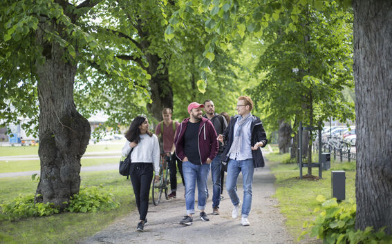 Unga vuxna går och pratar på en trädklädd parkstig med cyklar i bakgrunden