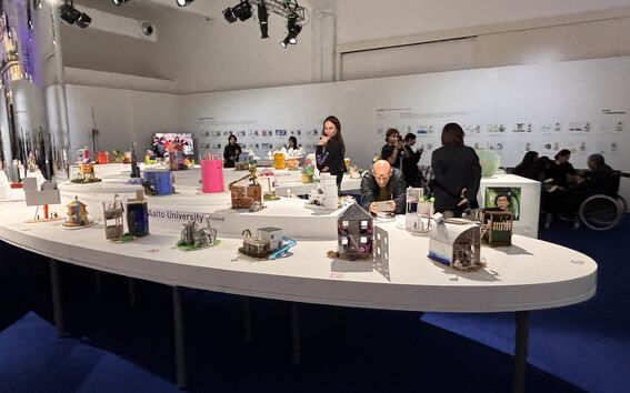 Colourful architectural models on a large white table in an exhibition hall