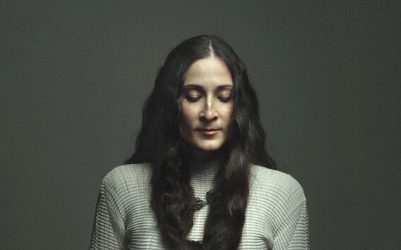 Person with very long dark hair in a braid, white textured top, holding small objects in both hands