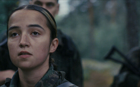 Soldiers in camouflage in a forest, face of a female soldier in the foreground