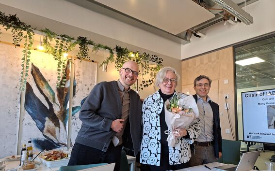 Two smiling men and a woman holding a bouquet of flowers.