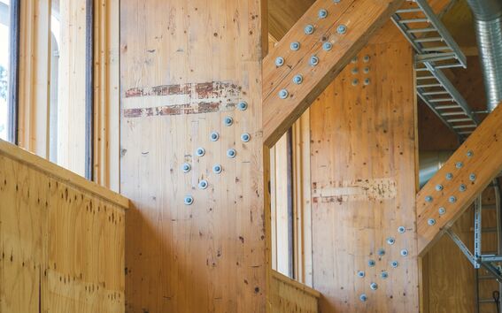 Interior with light timber beams and metal bolts, showing a wooden structure with exposed ducts and ladder.