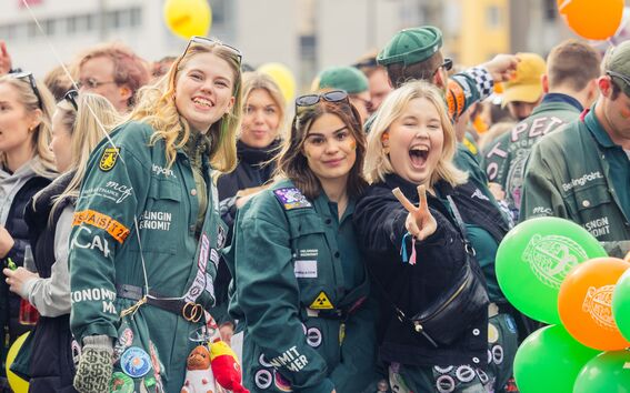 Students in green overalls at a lively outdoor event, posing for photos among orange and green balloons
