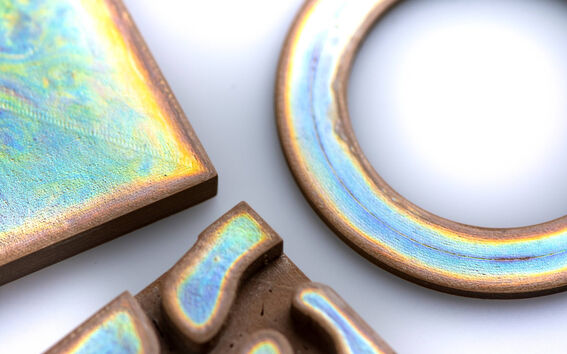 Close-up of brown ceramic pieces with iridescent blue and yellow glazed surfaces on a light background.