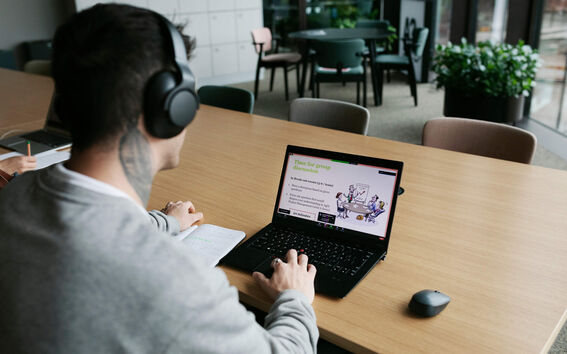 Person with headphones at a long table studying group discussion slides on a laptop in a modern room