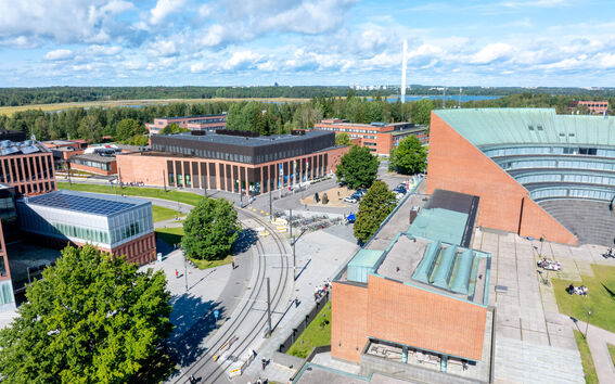 Aerial view of a modern campus with red brick buildings, tram tracks and green trees on a sunny day