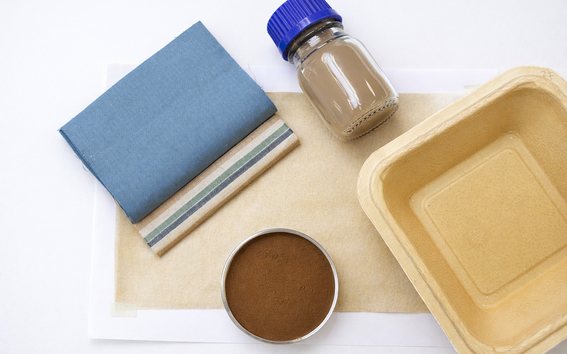 Blue and striped cloth, brown powder, beige tray and jar on light paper background