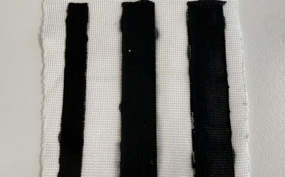 Three vertical black bars painted on a frayed white fabric rectangle on a pale surface