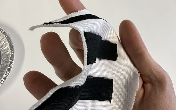 Hand holding curved white fabric strip with three black rectangular patches on a light surface