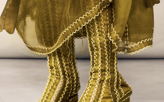 Person in golden knee-high heeled boots with ornate wavy trim and matching sheer layered skirt