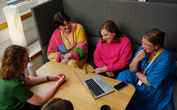 Five adults in bright clothes sit around a small table smiling.