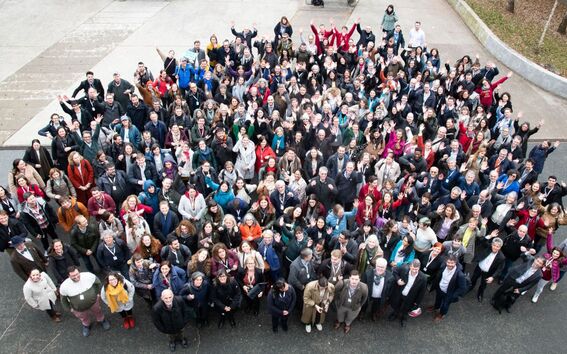 Large diverse crowd outdoors, looking up and waving, dressed in colourful winter clothes