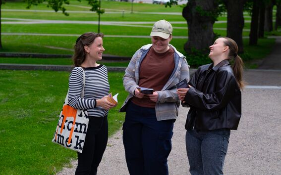 Design students Taija Piikkilä, Kasi Jutila and Leena Hurtig chatting in a green park, holding a friend book.