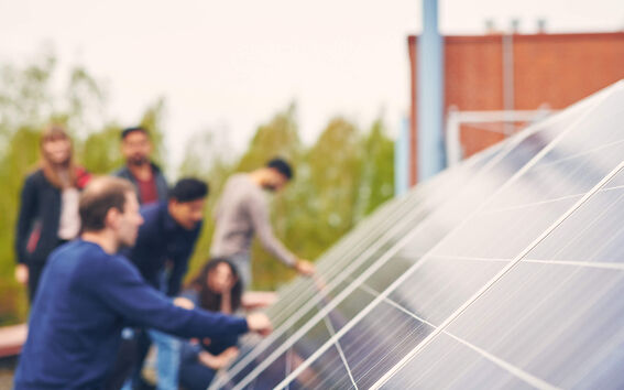 Group of people outdoors examining large blue solar panels on a rooftop