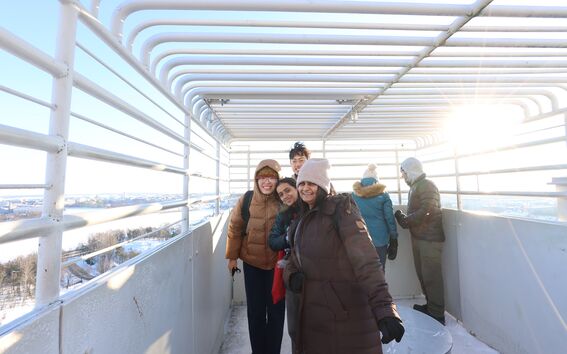 Smiling people in winter coats on a viewing deck of Olympic Stadium Tower and snowy landscape in bright sunlight
