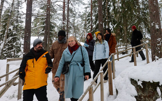 Smiling group walks down a snowy forest path with tall pine trees and wooden railings