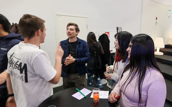 Four young adults chatting around a black table with drinks and handmade postcards
