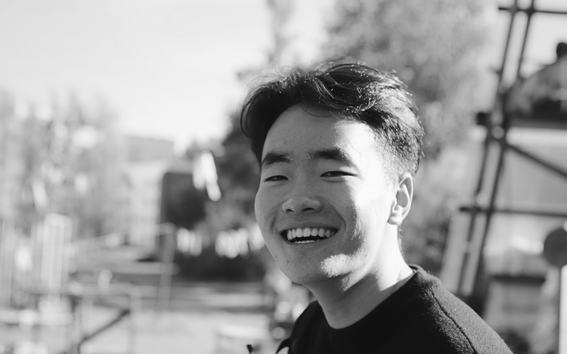 Smiling young person outdoors in black and white, with a blurred urban park scene in the background