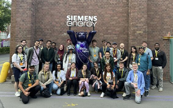 Group of people posing by a purple bear statue at Siemens Energy, against a brick wall