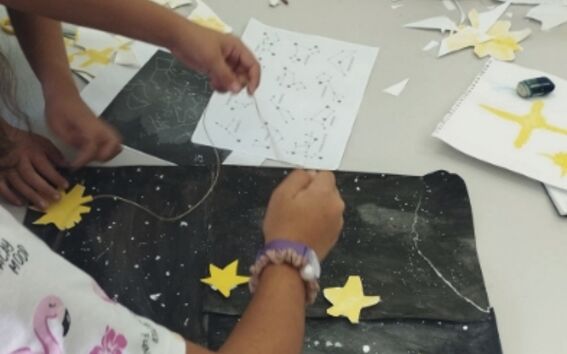 Children craft a starry night collage, gluing yellow stars onto a large black paper sky