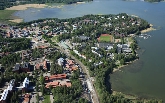 Aerial view of a lakeside campus with red and white buildings, sports field and forested shoreline