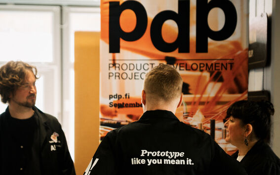 Aalto Design Factory’s three staff members stand in front of a Product Development Project banderol
