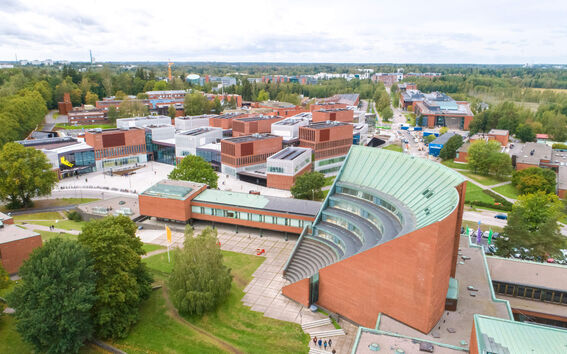 Aerial view of a red-brick university campus with a curved green-roofed hall among trees