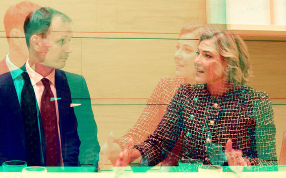Double exposure of man in suit and woman in patterned jacket talking at a light wood meeting table
