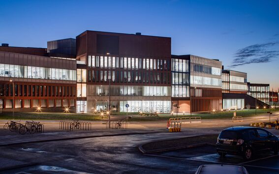 Modern glass and brick office building lit up at dusk, with parked cars and bicycles in front