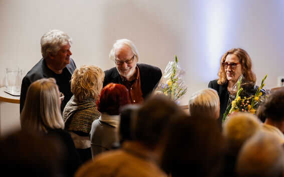 Smiling people in an auditorium audience, the person being celebrated holding a bouquet of flowers.