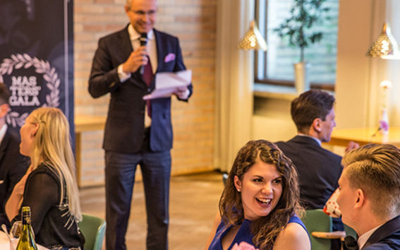 Taustalla Riku Asikainen pitämässä puhetta maistereille. Kuva: Joel Leinonen