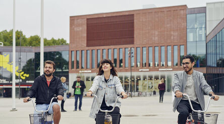 Kolme opiskelijaa pyöräilemässä kauppakeskus ABlocin edustalla