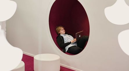 Opiskelija työskentelee tietokoneella maaten selällään pyöreässä valkoiseen seinään tehdyssä istumareiässä. Kuva: Aalto-yliopisto / Unto Rautio