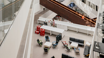 Modern interior with a large staircase, a lounge area with colourful chairs, and people near a counter.