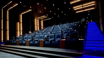 An empty modern movie theater with rows of blue lounge chairs, wall lights, and stairs highlighted with blue LED lights.