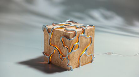 Puisesta kuutiosta tehty lamppu, hopeiset metallikuviot ja uria pitkin hehkuva lämmin oranssi valo