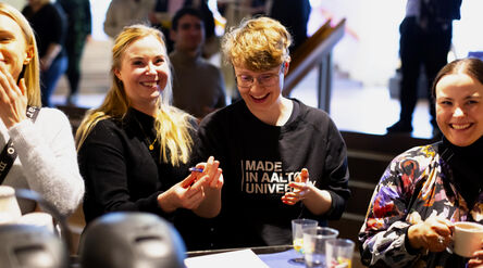 Unga vuxna samtalar runt ett bord med drycker på ett inomhusevenemang, ansiktena är suddade
