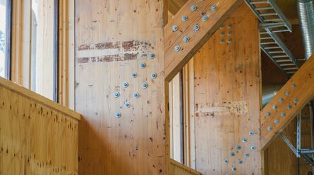 Interior with light timber beams and metal bolts, showing a wooden structure with exposed ducts and ladder.