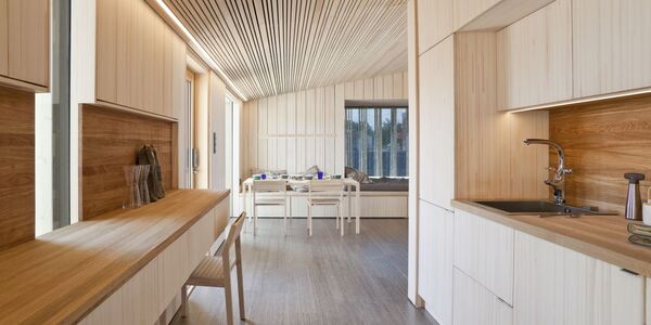 Modern kitchen with light wood cabinets, a dining area, and large window. Sleek design with wooden ceiling and floor.