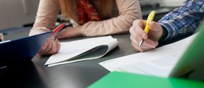 Close-up of two students making notes to research articles that they are reading.