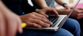 A man typing with a laptop on their lap. Only showing their arms and the laptop on their lap. Photo by Aalto University