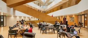 People studying in the School of Business main building with a large staircase in the background.