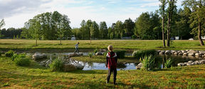 Kaksi poikaa leikkimässä ilta-auringossa kaupungin viheralueella, jonka keskellä on pieni lampi ja sen ympärillä kiviasetelma.