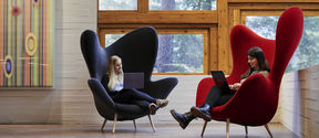 Two students are sitting in large, colourful chairs inside Dipoli
