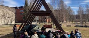Color photo of 15-17 attendees at an outdoor workshop at an A-frame building