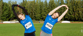 Two people stretching on a university's sports field. 