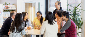 Smiling people sitting and standing around a table.