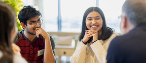 Students sitting by a table smiling.