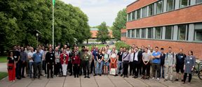 A group of several dozen people pose for a photo outside at Aalto University.