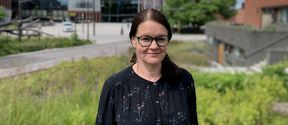 Dark-haired woman in dark dress standing outdoors with Otaniemi campus on a summer day